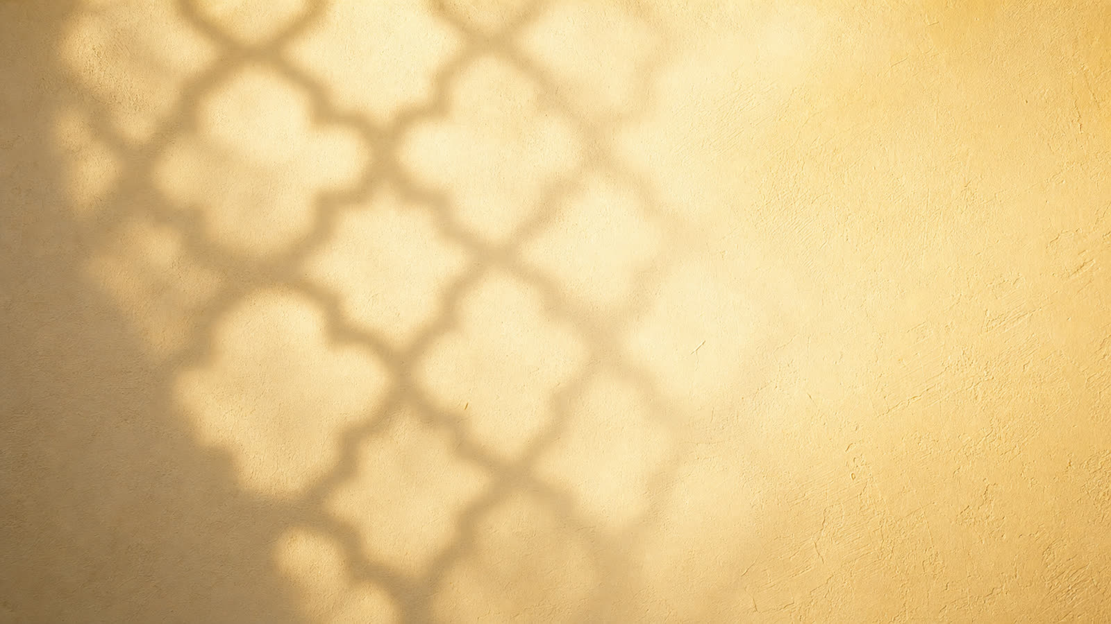 Soft geometric lattice shadow falling across a warm plaster wall